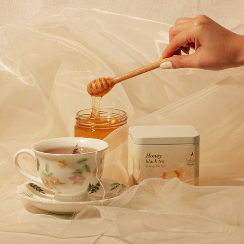 Honey Black Tea tin beside brewed tea and a jar of honey.