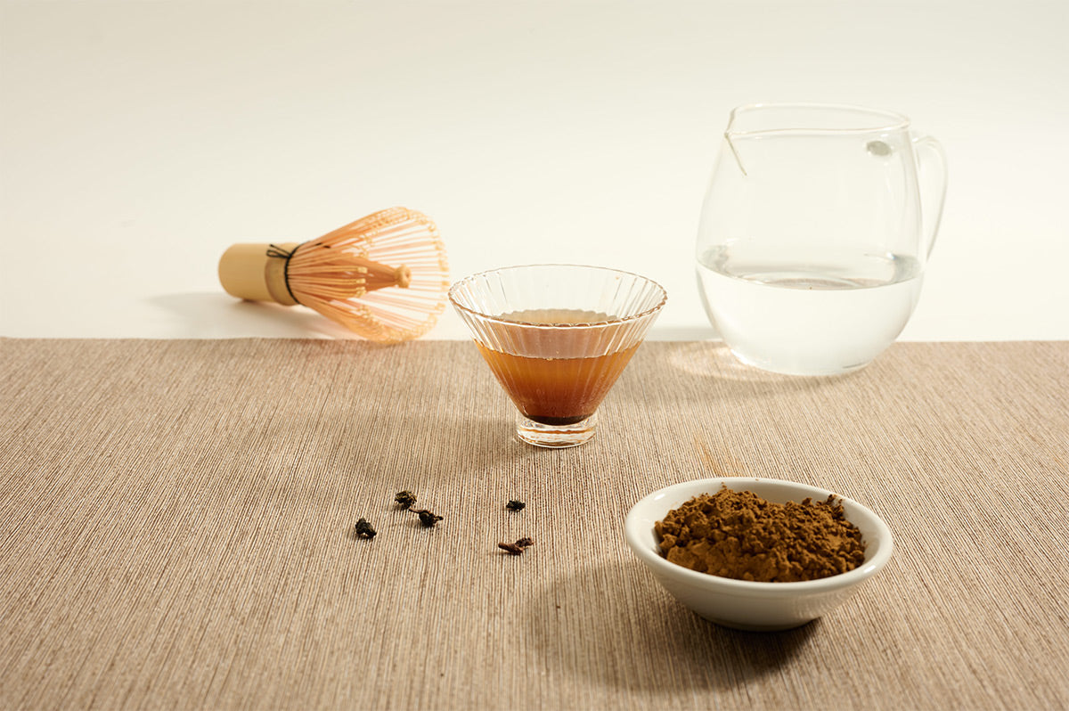 Ruby Black Tea Powder beside brewed tea and bamboo whisk. 